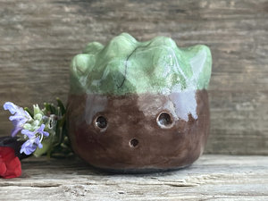 a roundish raku scuplture glazed in warm brown with green for the chestnut spikes on the top of its head. (they're not sharp at all!). it has a cute, open, friendly face.