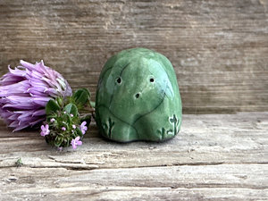 a small and stout nature spirit raku sculpture glazed in green. it has a cute little face, and a little plant carving on its right side.