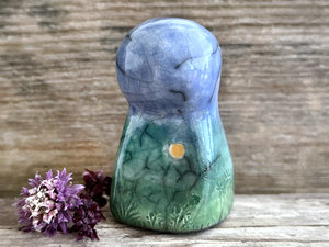 Raku ceramic earth spirit sculpture glazed in spring green, forest green, and blue (bottom to top). It has plant shapes and flowers carved into her and a yellow sun carving too.