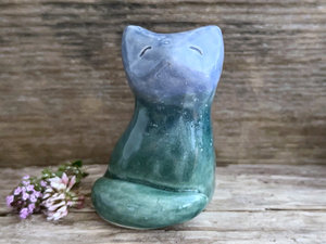 Raku ceramic earth and sky sitting kitsune fox sculpture glaze in a bottom-to-top gradient of forest green to blue. Its tail is curled around its body on the left, and it has a gentle, kind face.