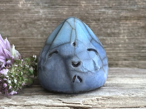 A small raindrop raku ceramic sculpture glazed in a gradient of blue to turquoise (bottom to top) with a smiley face. A prayer to end the droughts and floods.