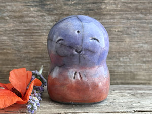 A smiley and loving Jizo Shinto raku ceramic sculpture talisman glazed in a bottom-to-top gradient of burnt orange to mauve to violet to blue. It has a kind, gentle face and is a wonderful smooth shape to hold in the hand.
