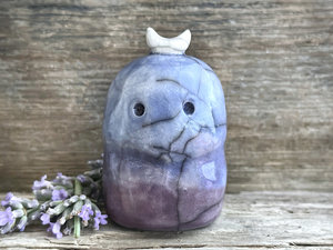 A kodama nature and forest spirit kami ceramic raku sculpture glazed in a bottom-to-top gradient of soft purple to blue. It has a gentle face, and a white crescent moon on its head.