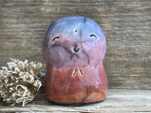 A smiley and loving Jizo Shinto raku ceramic sculpture talisman glazed in a bottom-to-top gradient of red-orange to mauve to purple to blue. It has a kind, gentle face and is a wonderful smooth shape to hold in the hand.