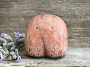 a small and stout nature spirit raku sculpture glazed in peach. it has a cute little face, and little plant carvings on its front.