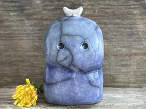 A kodama nature and forest spirit kodama kami ceramic raku sculpture glazed in a bottom-to-top gradient of darker to lighter blue. It has a gentle face, and a white crescent moon on its head.