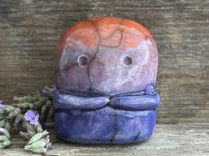 A kodama nature spirit ceramic guardian statue glazed in a bottom-to-top gradient of indigo to violet to mauve to red-orange. It has a wide face, two big eyes, and cute little arms.