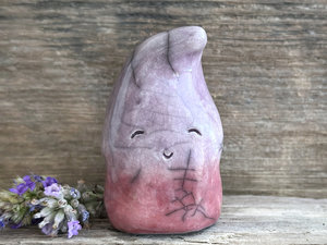 raku ceramic gnome spirit glazed in a bottom-to-top gradient of soft bordeaux red to purple. it has a happy, gentle, kind face, and the top of its head is curled over, a little like it's wearing a nightcap.