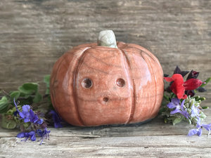 Raku ceramic pumpkin nature spirit kami sculpture glazed in a red-orange colour. it has a small, pale green-brown stem and a cute, slightly surprised and worried-looking ooooo face.