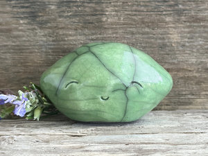 a very happy raku ceramic sculpture of a lime or a green lemon. it's glazed in a soft bright green colour.