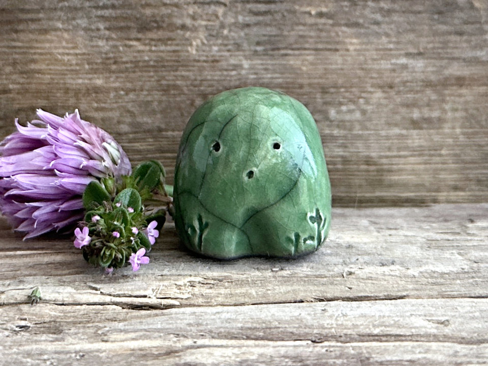 a small and stout nature spirit raku sculpture glazed in green. it has a cute little face, and a little plant carving on its right side.