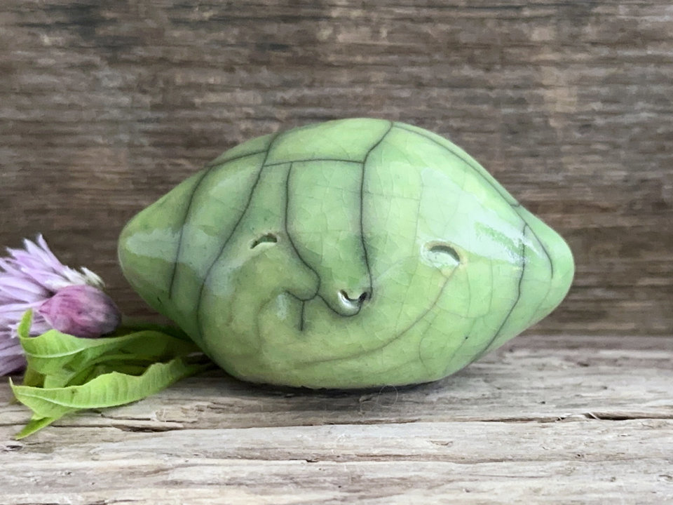 a very happy raku ceramic sculpture of a lime or a lemon. it's glazed in a pale bright green colour.