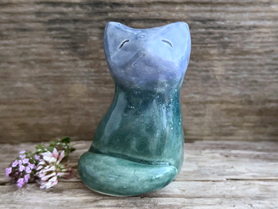 Raku ceramic earth and sky sitting kitsune fox sculpture glaze in a bottom-to-top gradient of forest green to blue. Its tail is curled around its body on the left, and it has a gentle, kind face.