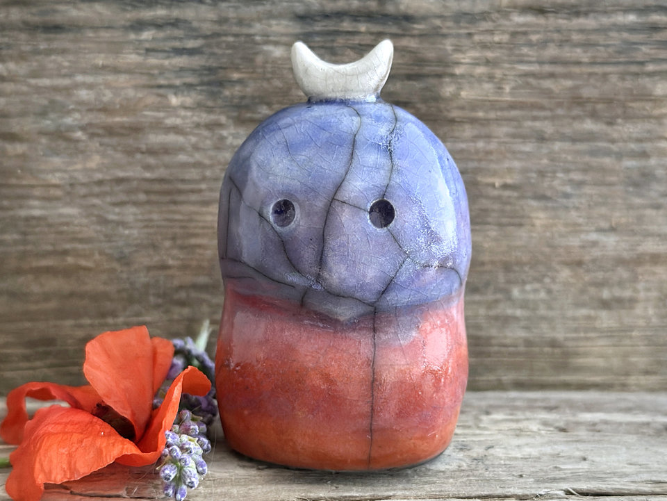 A kodama nature and forest spirit kodama kami ceramic raku sculpture glazed in a bottom-to-top gradient of red-orange to mauve to purple to indigo. It has a gentle face, and a white crescent moon on its head.