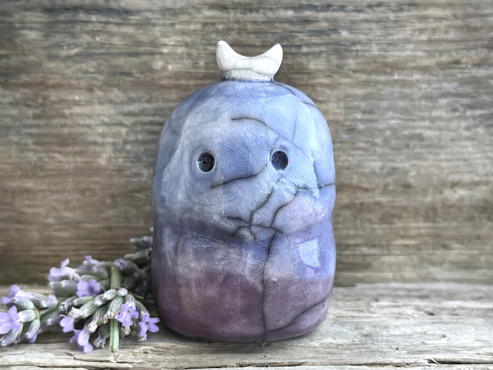 A kodama nature and forest spirit kami ceramic raku sculpture glazed in a bottom-to-top gradient of soft purple to blue. It has a gentle face, and a white crescent moon on its head.