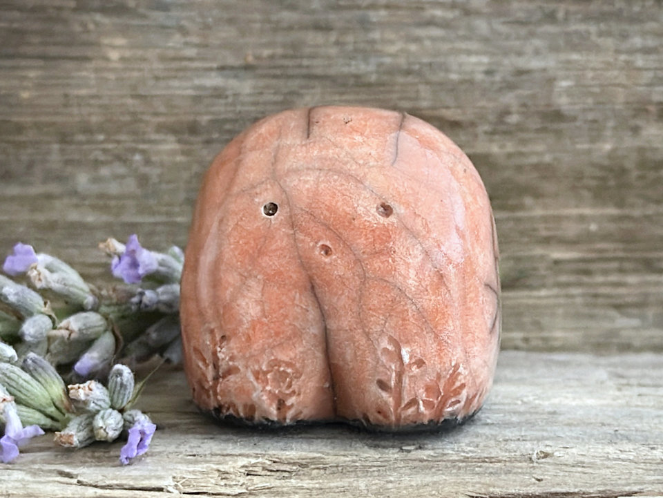 a small and stout nature spirit raku sculpture glazed in peach. it has a cute little face, and little plant carvings on its front.