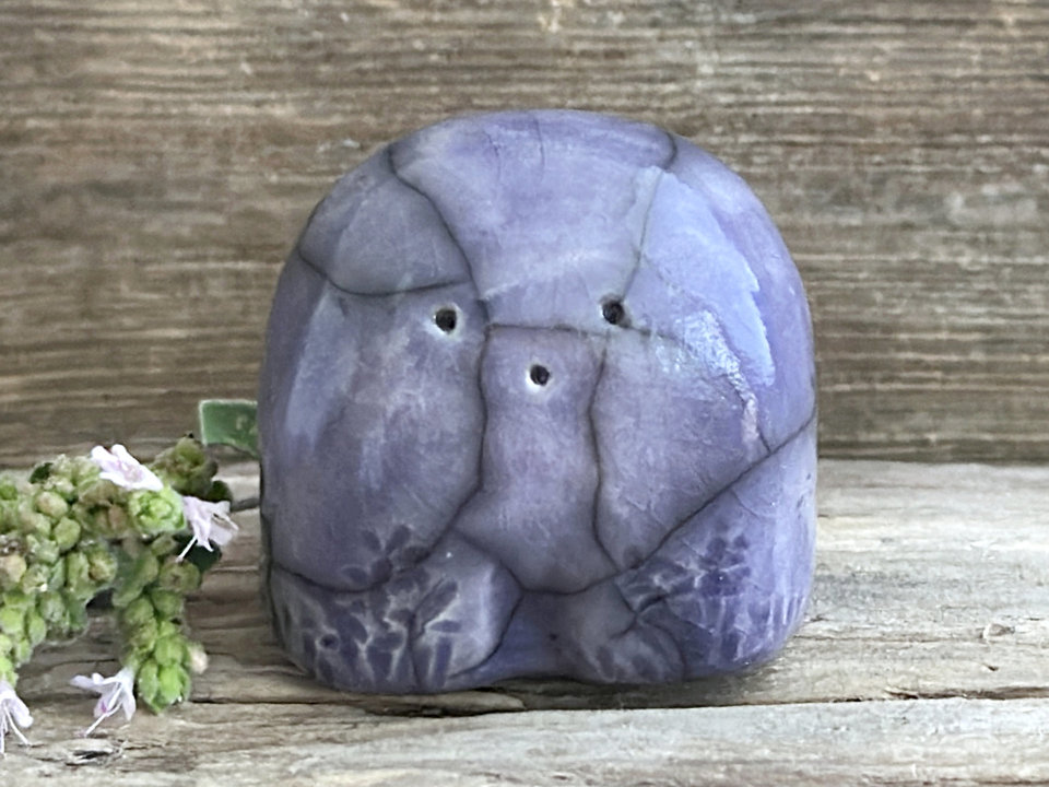 a small and stout nature spirit raku sculpture glazed in indigo-violet. it has a cute little face, and little plant carvings on its front.
