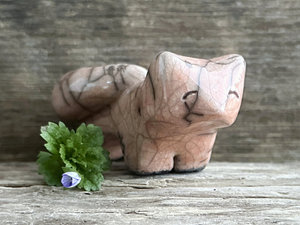 Raku ceramic kitsune fox sculpture glazed in a soft warm peach colour. It has a kind, gentle face, and a tail curled over its back. There are tiny dark grey spiderweb patterns in the glaze, in addition to the normal raku crackles, from where raindrops fell on it.