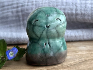 a smiley and loving Jizo Shinto raku ceramic sculpture talisman glazed in forest green and brown (at the bottom). they have a kind, gentle face and are a wonderful smooth shape to hold in the hand.