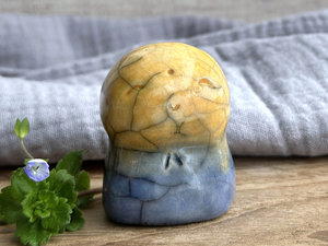 a smiley and loving Jizo Shinto raku ceramic sculpture talisman glazed in a bottom-to-top gradient of blue to golden yellow. they have a kind, gentle face and are a wonderful smooth shape to hold in the hand.