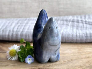 raku ceramic creature glazed in a front-to-back gradient of pale blue-grey to a darker, more intense blue colour. it has four stubby legs and both its front and back ends rise up to a point, so that when you look at it from the side, it almost looks like a pair of horns. it has a small, cute face.