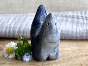 raku ceramic creature glazed in a front-to-back gradient of pale blue-grey to a darker, more intense blue colour. it has four stubby legs, and both its front and back ends rise up to a point, so that when you look at it from the side, it almost looks like a pair of horns. it has a small, cute face.