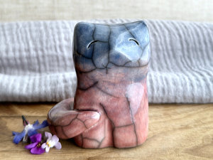 A calm and gentle Shinto Inari nighttime kitsune fox spirit ceramic raku statue glazed in a bottom-to-top gradient of soft pink-orange-red to mauve to blue. Its tail is curled around the right side of its body, and it has a kind face.