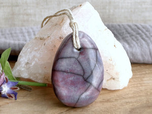 Raku ceramic sculpture shaped a little like a bendy pear and glazed in a mix of violet and mauve. It is strung on a hemp cord.