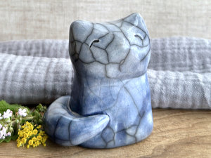 A calm and gentle Shinto Inari moon-gazing kitsune fox spirit ceramic raku statue glazed in a bottom-to-top gradient of blue to pale blue. Its tail is curled around the right side of its body, and it has a kind face. Its head it tilted ever so slightly up.