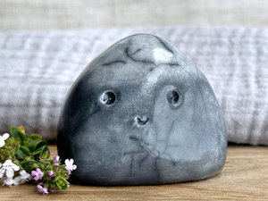 small cloud raku ceramic sculpture glazed in a bottom-to-top gradient of grey to almost white at the top. it has a happy face and is shaped vaguely like a squat raindrop.