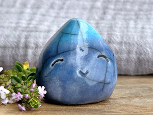 small raku ceramic raindrop sculpture glazed in a bottom-to-top gradient of blue to turquoise. it has a happy, smiling face and looks very contented.