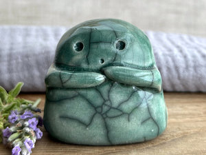 A sweet little kodama nature spirit ceramic guardian statue glazed in soft forest green and with a lovely, gentle face and little arms. they have some very small, dimpled, pinhole glaze disturbance marks on their back and side.