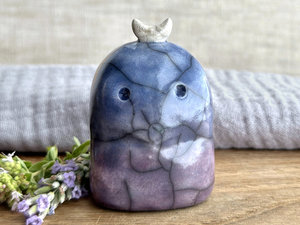 A kodama nature and forest spirit kami ceramic raku sculpture glazed in a bottom-to-top gradient of purple-violet to blue. It has a gentle face, and a white crescent moon on its head.