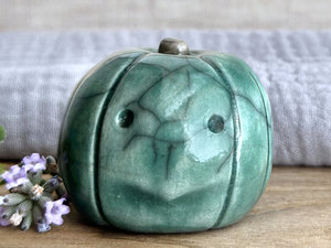 raku ceramic forest-green pumpkin nature spirit sculpture with a somewhat uncertain, intense and worried look on its face. it has a cute little green-brown stalk on top.