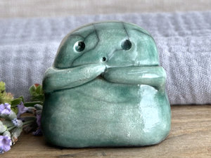 A sweet little kodama nature spirit ceramic guardian statue glazed in soft, pale forest green and with a lovely, gentle face and little arms.