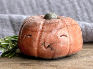 Raku ceramic orange pumpkin nature spirit kami sculpture with a very happy, smiley face. It has a small green-brown stem at the top.