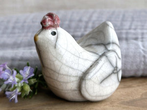 a white raku ceramic chicken with grey eyes, a pale orange beak, and a bordeaux red comb on the top of her head. she looks very sweet.