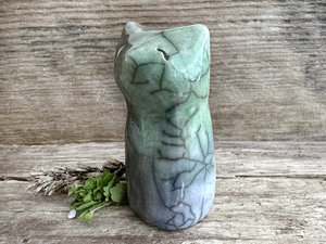 Raku ceramic earth and water spirit kitsune sitting fox sculpture glazed in green, grey, and blue. It is sitting up with its tail curled up its back, and it has a gentle, kind face.