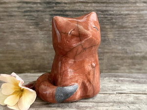A wise and contented Shinto Inari sitting kitsune fox kami spirit ceramic raku statue glazed in a deep burnt-orange colour. The tip of its tail is unglazed black.
