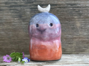 A kodama nature and forest spirit kami ceramic raku sculpture glazed in a bottom-to-top gradient of burnt red-orange to mauve to purple to indigo. It has a gentle face, and a white crescent moon on its head.