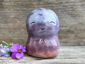A smiley and loving Jizo Shinto raku ceramic sculpture talisman glazed in a bottom-to-top gradient of burnt orange to mauve to violet-blue. It has a kind, gentle face and is a wonderful smooth shape to hold in the hand.