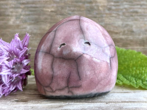 a small, kind of dome or egg-shaped raku ceramic sculpture of a woodland nature spirit. it's low to the ground and with a gentle face and little nose. it's glazed in a dusky purple-mauve colour.