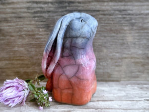 Raku ceramic usagi rabbit kami nature spirit glazed in a bottom-to-top gradient of burnt orange to mauve to indigo-violet. Its ears are folded down its back, and it has a kind, gentle face.