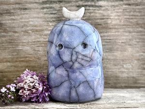 A kodama nature and forest spirit kami ceramic raku sculpture glazed in blue with faint hints of mauve. It has a gentle face, and a white crescent moon on its head.