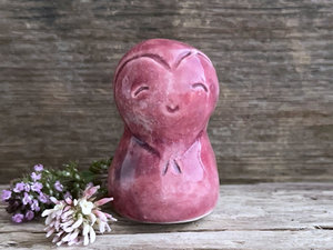 A smiley and loving Jizo Shinto raku ceramic sculpture talisman glazed in warm, pinky red colour with hints of purple. It has a heart shape carved around its kind, gentle face and is a wonderful smooth shape to hold in the hand.