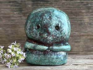 A kodama nature spirit ceramic guardian statue glazed in a turquoise and copper glaze. It has a wide face, two big eyes, and cute little arms.
