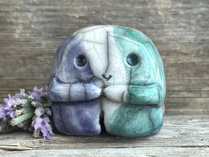 A sweet little nature spirit ceramic guardian statue glazed in the men's gay flag green, white, and blue colours and with a lovely, gentle face and little arms. It has a small branch design carved up one side.