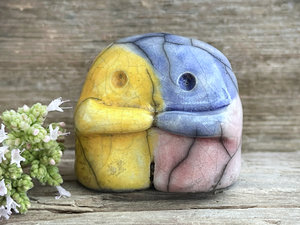 A sweet little nature spirit ceramic guardian statue glazed in the pansexual flag blue, yellow, and pink colours and with a lovely, gentle face and little arms. It has a small branch design carved up one side.