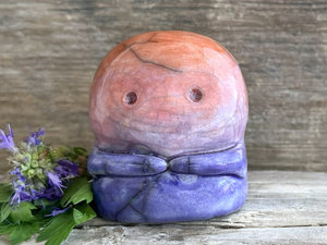 A kodama nature spirit ceramic guardian statue glazed in a bottom-to-top gradient of indigo to violet to mauve to red-orange. It has a wide face, two big eyes, and cute little arms.