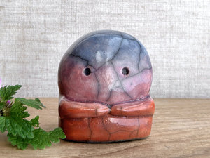 A kodama nature spirit ceramic guardian statue glazed in a top-to-bottom gradient of blue to violet to mauve to red-orange. It has a wide face, two big eyes, and cute little arms.